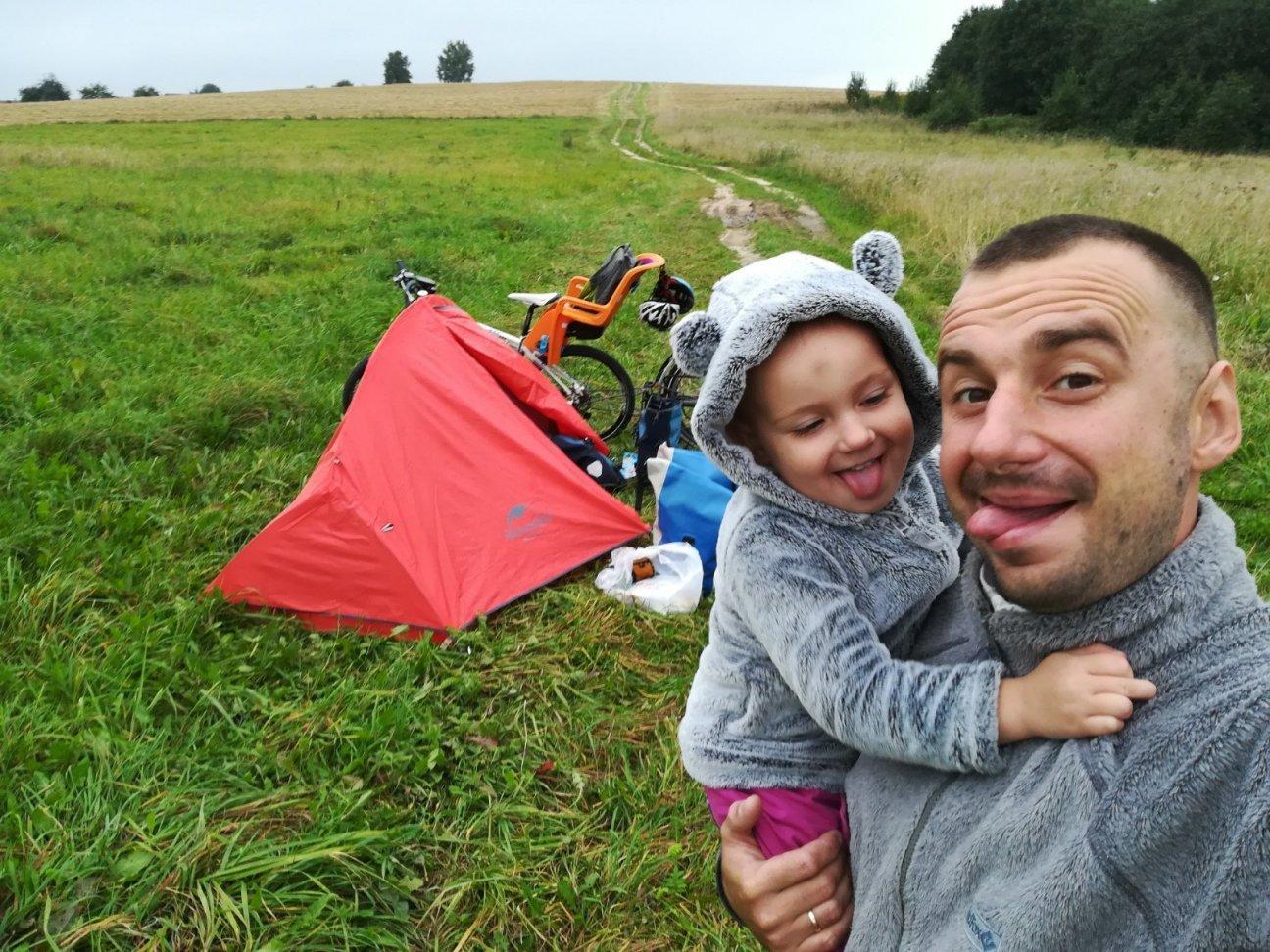 Счастливый папа и дочурка возле палатки и велосипеда в поле