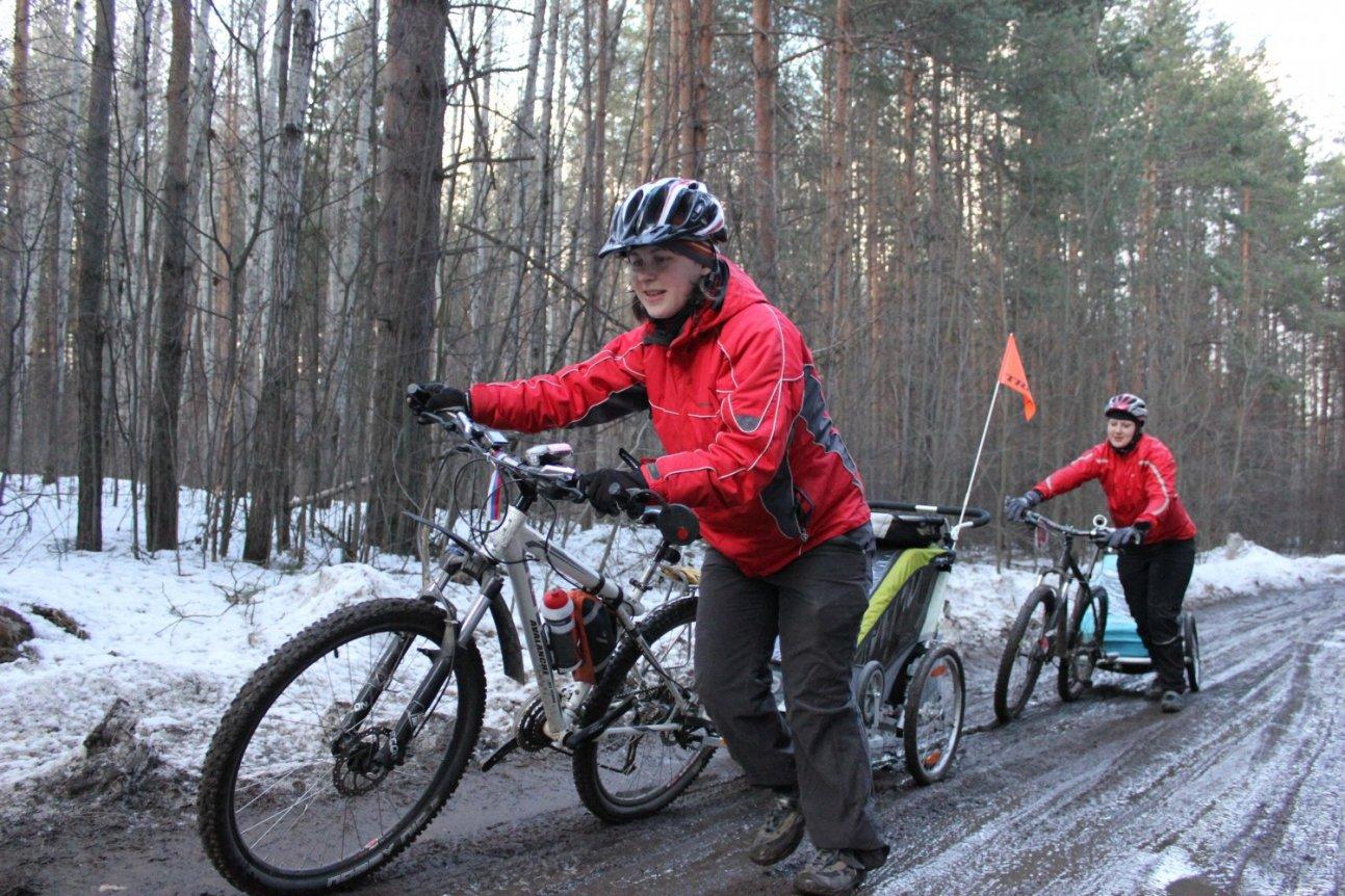 Женщины на велосипедах с велоприцепами и детьми по грязи