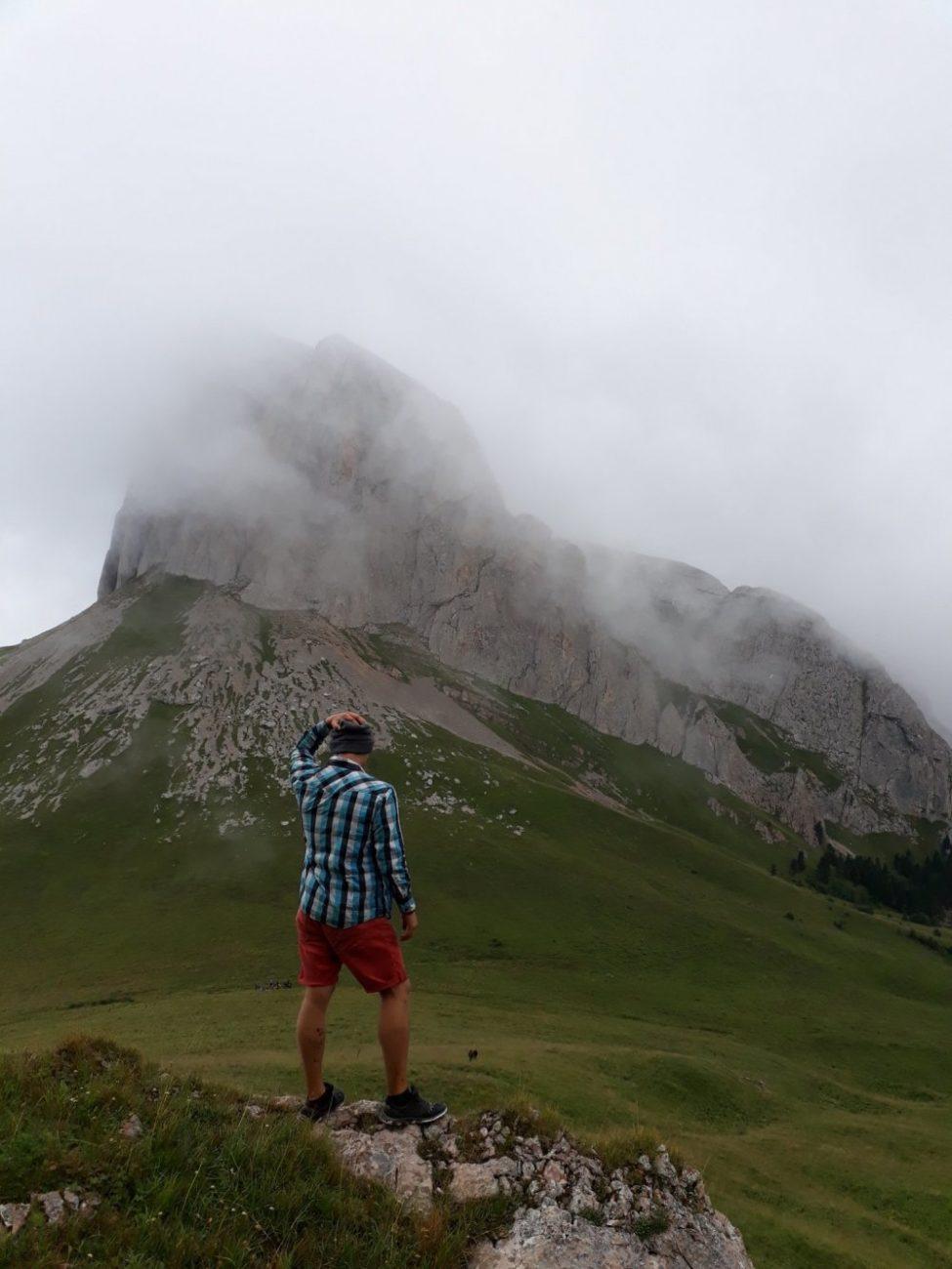 Молодой человек в горах стоит спиной на фоне скалы