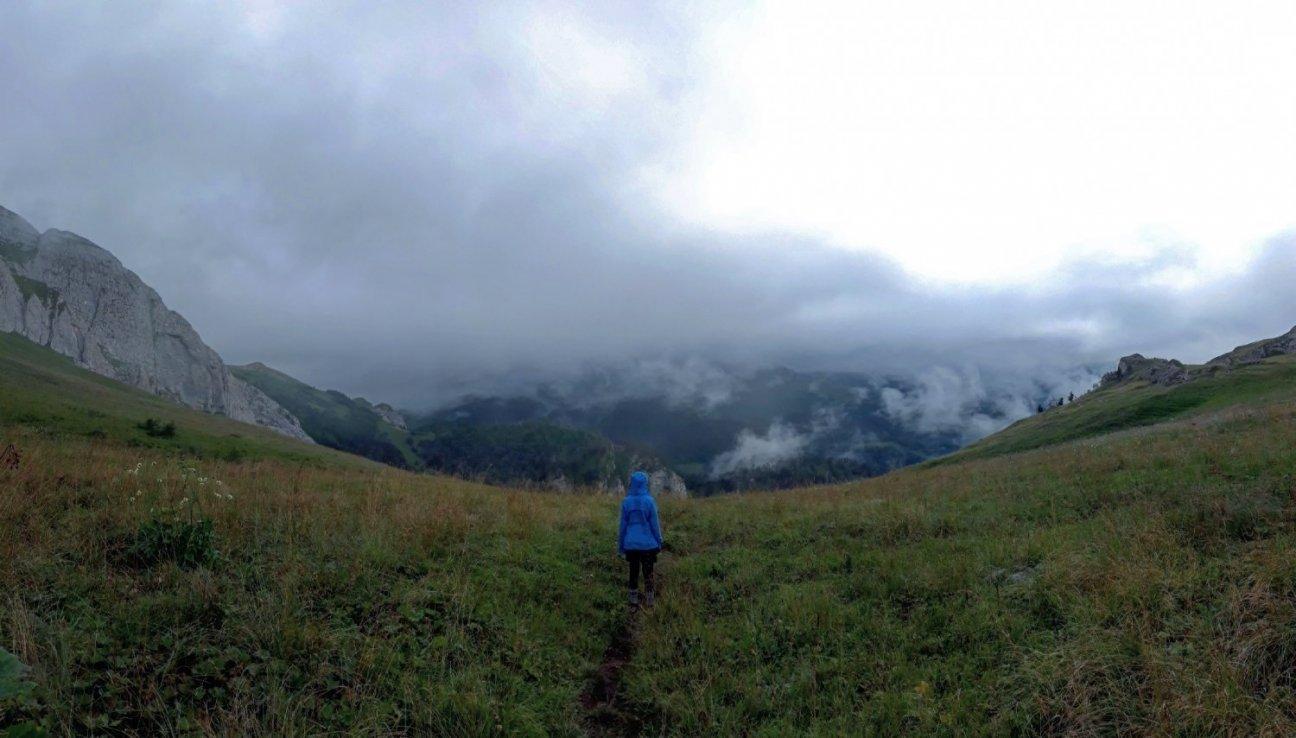 Девушка высоко в горах стоит и смотрит в даль, туман, облака