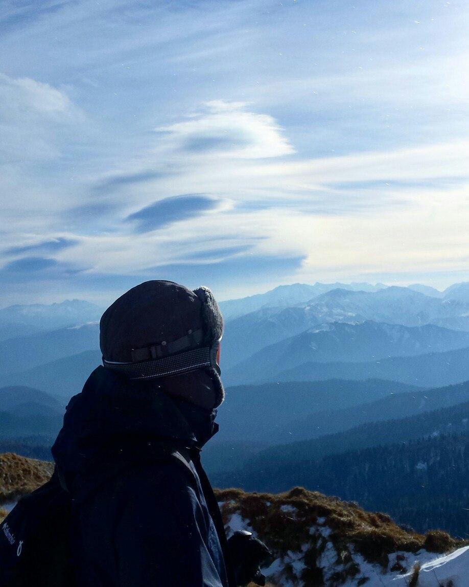 молодой человек смотрит далеко в горы, в шапке и горнолыжных очках