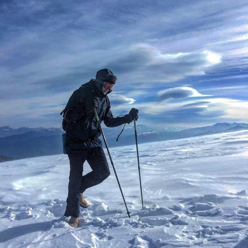 высоко в горах молодой человек поднимается с трекинговыми палками, много снега