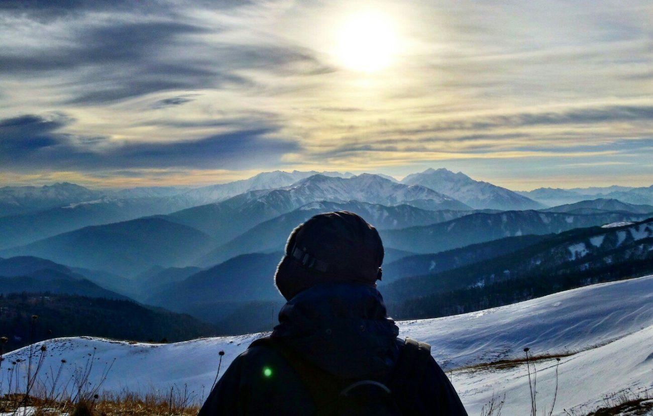 Человек спиной к фотоаппарату на фоне снежных красивых гор на закате