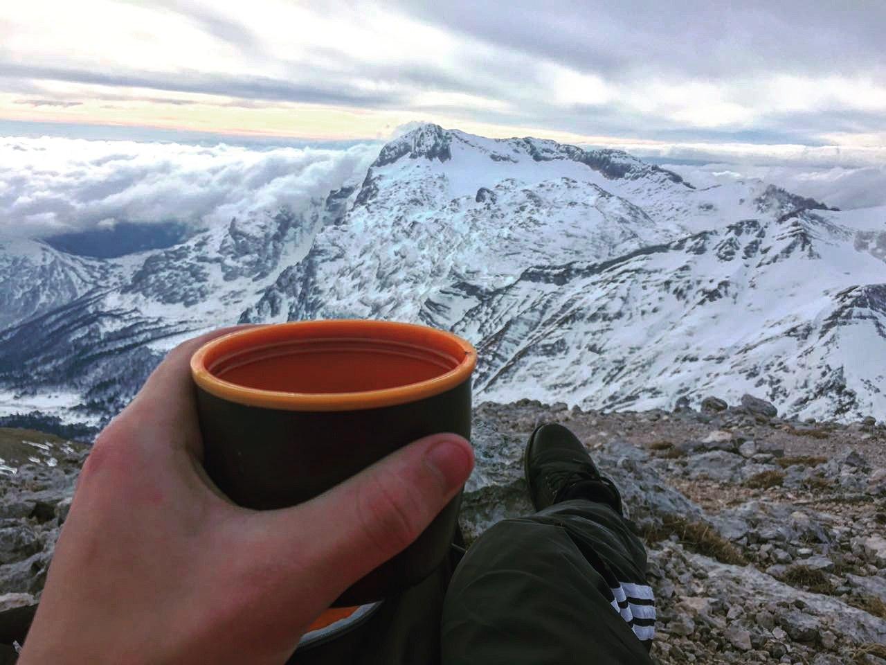 Человек в горах держит чашку с чаем и пьет